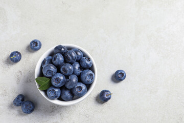 Bowl of fresh tasty blueberries on light grey table, flat lay. Space for text