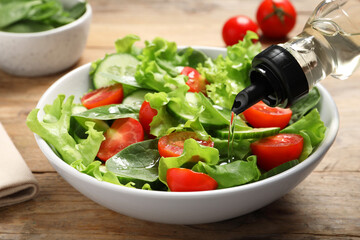 Pouring oil into delicious vegetable salad on wooden table, closeup