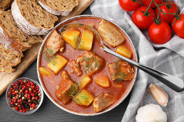 Delicious goulash in bowl, bread and ingredients on dark wooden table, flat lay