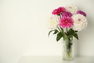 Bouquet of beautiful Dahlia flowers in vase on table near white wall, space for text