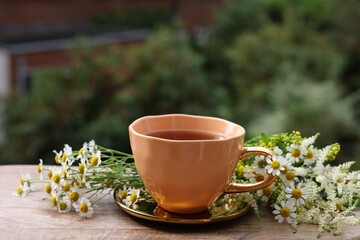 Cup of delicious chamomile tea and fresh flowers outdoors