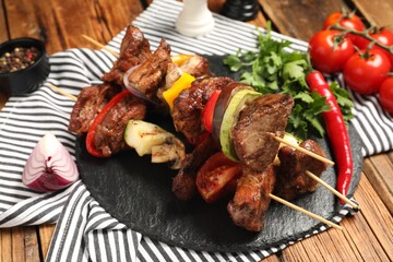 Delicious shish kebabs with vegetables on wooden table