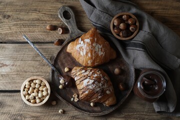 Delicious croissants with chocolate and nuts on wooden table, flat lay