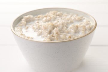 Tasty boiled oatmeal in bowl on white table, closeup
