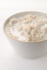 Tasty boiled oatmeal in bowl on white table, closeup