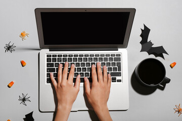 Female hands with laptop, cup of coffee and Halloween decorations on grey background