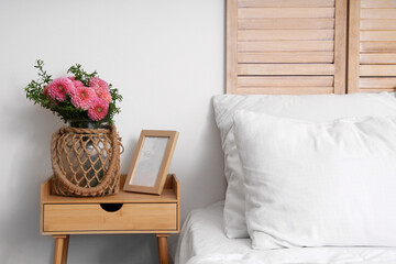 Wicker vase of beautiful pink dahlias with frame on bedside table in bedroom