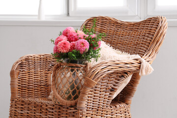 Fototapeta na wymiar Vase of beautiful pink dahlias on wicker chair in bedroom