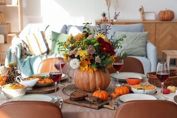 Pumpkin with autumn bouquet on festive dining table in room, closeup