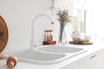 White counter with sink, condiments and dried flowers in interior of modern kitchen