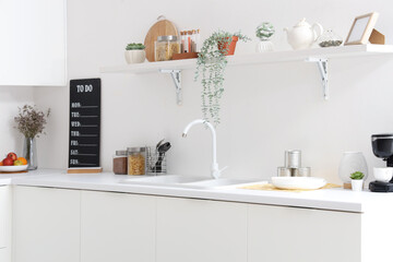 Interior of light kitchen with white counters, shelf, sink and utensils