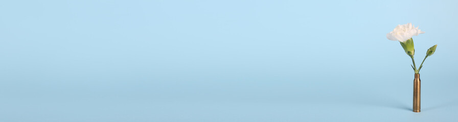 Bullet cartridge case with beautiful carnation flower on light blue background, space for text. Banner design