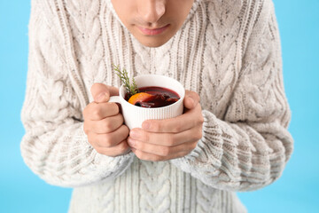 Man with mug of warm mulled wine on blue background, closeup
