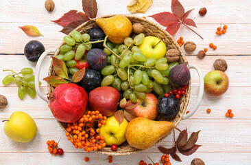 Wicker basket with different fresh fruits on white wooden background