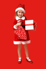 Cute little girl in Santa Claus costume with gift box and bag on red background