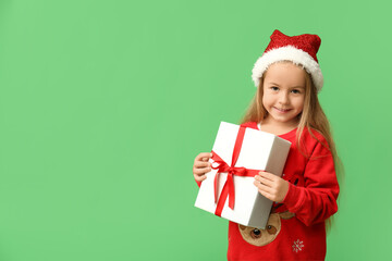 Cute little girl in elf costume with gift box on green background