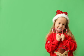 Cute little girl in elf costume with candy canes on green background
