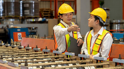 Factory worker operating metal stamping machine while supervised by engineer for optimal quality...