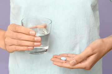 Woman with pills and glass of water on lilac background, closeup