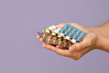 Female hands with pills in blister packs on lilac background, closeup
