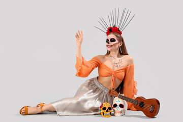 Young woman with painted skulls and guitar on grey background. Celebration of Mexico's Day of the...