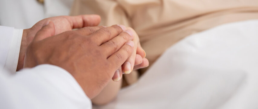 Closeup hands of doctor man encourage with elderly patient at the hospital, physician take care and holding hands for consoling senior sick, diagnostic disease and illness, medical concept.