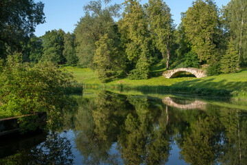 View of the Apollo Bridge on the bank of the Facade Pond on the Slavyanka River in Pavlovsky Park on a sunny summer day, Pavlovsk, St. Petersburg, Russia