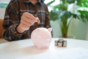Saving money. hand putting money into pink piggy bank making investments or strategy for personal...