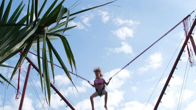Little girl having fun while bungee jumping in amusement park, summer holidays and vacation concept