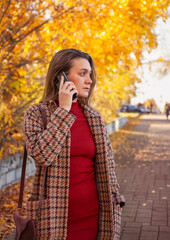 Beautiful young woman talking on the phone in autumn park