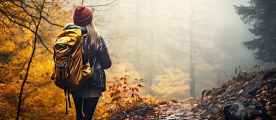 Female tourist capturing nature s beauty while hiking through a foggy fall forest with her camera and backpack - obrazy, fototapety, plakaty