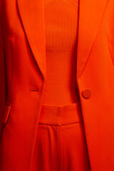 Bright orange clothing including pants, a blazer and a top are seen displayed on a mannequin. 