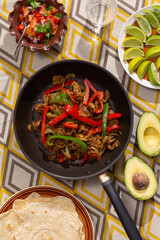 Quesadilla ingredients including avocado, lime, meat, capsicum and tomato salsa sit atop a vintage patterned table cloth in soft directional sunlight.