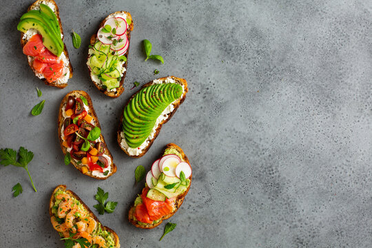 Healthy breakfast toasts with avocado, salmon, cucumber, radish, cherry tomatoes and herbs. Copy space