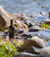 Wine Bottle and Red Wine Glass Next to a River with Rocks