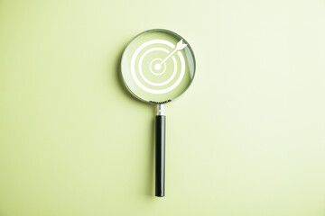 Features a target board captured inside a magnifier glass, illustrating the focus on business objectives, target search concept, and attaining success. Isolated on a background with copy space.