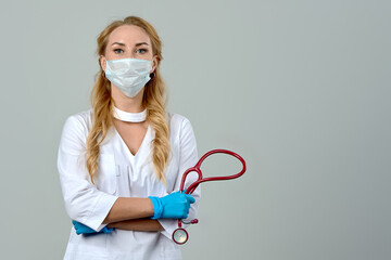 a female doctor in a white coat and a medical mask, wearing blue gloves with a stethoscope in her...