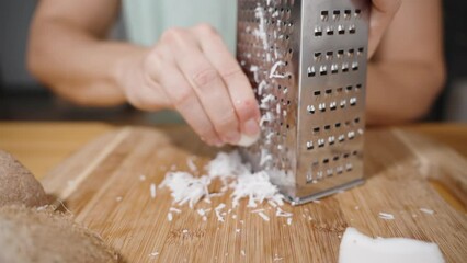 Close-up of Coconut Pieces, and the Woman Grating Them on a Metal Grater, in slow motion. - Powered by Adobe