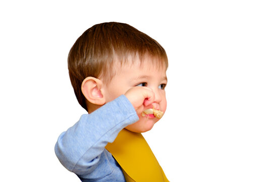 Toddler Baby Eats Porridge With A Spoon While Sitting At The Table On A Children S High Chair, Isolated On A White Background. Kid Aged One Year And Three Months