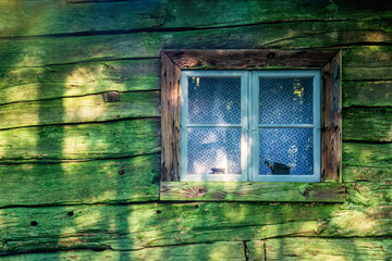 Window of an old wooden croft with green lichen on the wall - obrazy, fototapety, plakaty