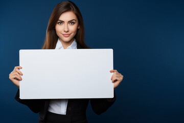 Naklejka premium Professional business woman holding a blank empty white color board in her hand on dark background, Young lady Holding Blank Placard, Happy positive blonde business woman holding a blank billboard