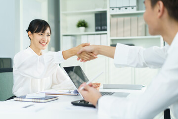 Fototapeta premium Two young Asian businesspeople having a handshaking together in office, man and woman shaking hand after finished their works.