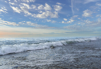 waves in a seascape at sunrise with a blue cloudy sky
