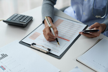 Confident female doctor, therapist sitting at table with medical stethoscope using laptop and mobile phone to write medical notes planning concept Study the treatment system Life insurance analysis.