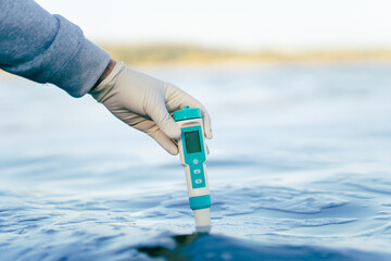 examination of water quality in natural reservoir. a device for measuring impurities in water in the male hand of a scientific specialist. - obrazy, fototapety, plakaty