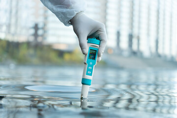 Electronic water testing hand over blurred blue water background, water quality check. testing the level of water pollution in a natural reservoir. - obrazy, fototapety, plakaty