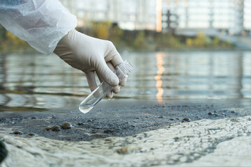 female ecologist in protective glove holding a test tube with water from a city river - obrazy, fototapety, plakaty