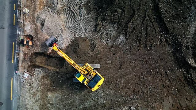 Drone top down descends on excavator removing wet dirt from construction site