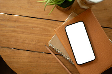 A white-screen smartphone mockup on a book on a wooden table. study table, office desk