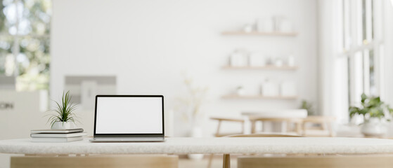 A tabletop with a white-screen laptop with a blurred modern white lobby room in the background.